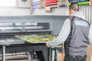 man printing in large format printer holding paper with hand