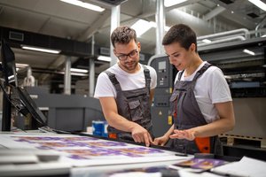 Two printing press workers checking graphics of printed material