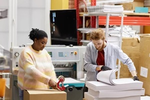portrait of two workers opening boxes with paper in industrial print shop